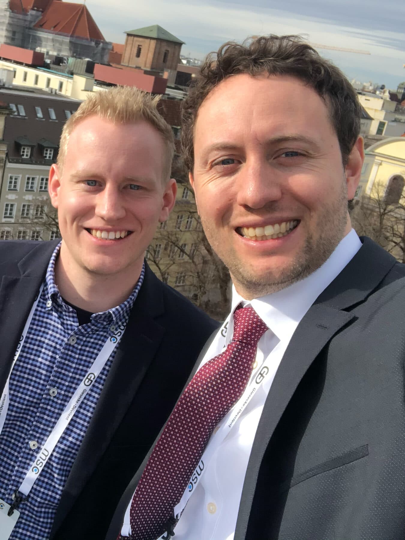 Sebastian Küsters und Marc Conzelmann, ein Selfie mit Konferenzbändern vor Dächern und Kirchtürmen der Münchner Altstadt